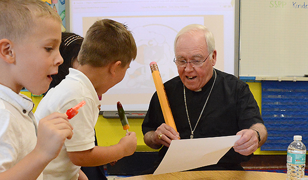 Bishop Richard J. Malone shows St. Peter and Paul School kindergartners how to write in cursive with a huge pencil during the first day of class  as the children try and beat the heat with ice pops at the Williamsville school. (Dan Cappellazzo/Staff Photographer)