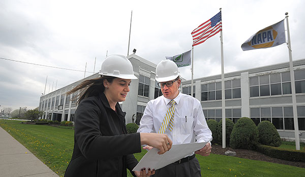 Framed by the former American Axle plant at 1001 East Delavan Ave., which will become the new education building for Catholic Charities, project manager Tess M. Williams looks over plans with Jeffrey Conrad, Catholic Charities director of workforce and education service, for the new facility. (Dan Cappellazzo/Staff Photographer)