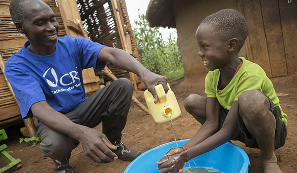 Kiplangat Hosea (right), 8, washes his hands during a hygiene sensitization session by Catholic Relief Services community mobilizer Akusuro John in Bukwo District, Uganda. CRS recently helped implement WASH (water, sanitation and hygiene) interventions in the village. (Jake Lyell/Catholic Relief Services)