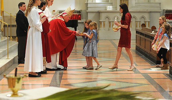 Framed by Palms and a vessel of Holy Water Bishop Richard Malone accepts the Gifts before Communion at St Joseph Cathedral during Palm Sunday Mass. (Dan Cappellazzo/Staff Photographer)