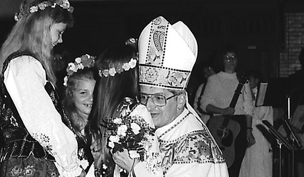 Bishop Edward M. Grosz is presented with flowers as he returns to celebrate Mass at his childhood parish, Assumption Church, on May 16, 1990.