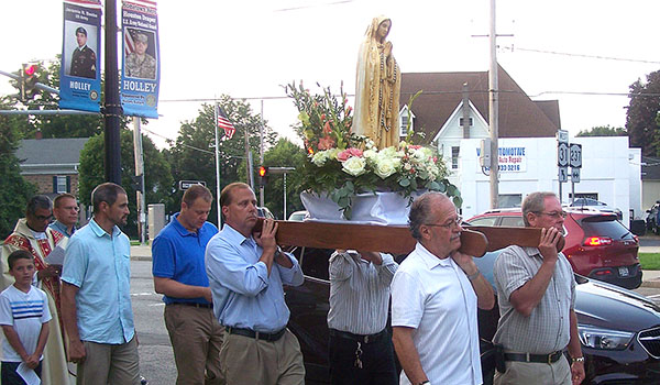 Four parishioners from St. Mary Parish in Holley carry a statue of the Virgin Mary as they lead a procession through the center of Holley for the Feast of the Assumption. The procession, which is a public display of the Catholic faith, takes place annually. (Patrick J. Buechi/WNYC Staff)