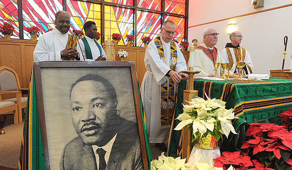 Bishop Richard J. Malone is flanked by a large portrait of Martin Luther King Jr. as he prepares the gifts during Mass. (Dan Cappellazzo/Staff Photographer)