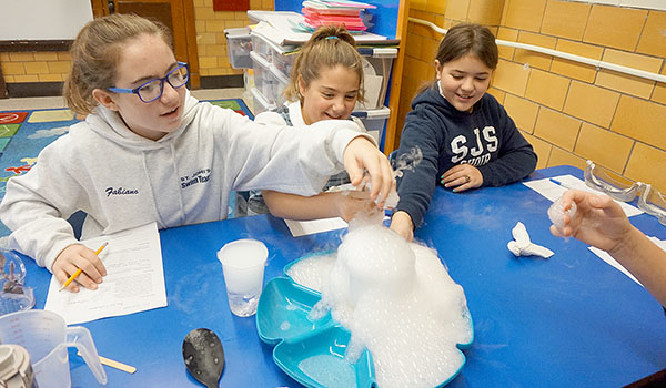 Fifth-grade students Ella Fabiano, Julia Crawford and Hailey Muff work with dry ice during a science lab experiment on states of matter. (Courtesy of St. John the Baptist)