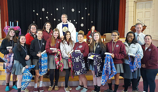 Eleven Sacred Heart students show off their chitenges, a traditional Zambian cloth, after being blessed by Father John Staak, OMI. The students are preparing for an immersion trip to Zambia this summer. (Courtesy of Sacred Heart Academy)