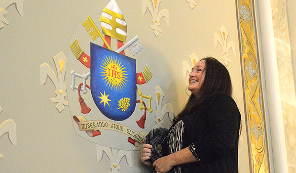 As St. Mary of the Angels celebrates the first year as a minor basilica with a special Mass and dedications, Jennifer Kane, communications director for the basilica, unveils Pope Francis's coat-of-arms on the sanctuary wall. (Patrick McPartland/Managing Editor)