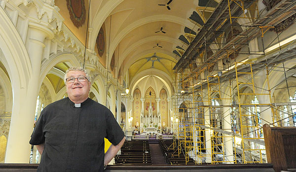 Father Gregory Dobson stands inside St. Mary of the Angels Church as workers put the final touches on the ceiling. (Patrick McPartland/Staff Photographer)