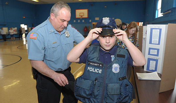 Patrolman Paul Nazzarett (left), Cheektowaga Police Department community crime prevention officer, helps fifth-grader Andrew Baker put on a bullet proof vest as Mary Queen of Angels students host a career fair where each student presents a career that they have researched. Students dressed up like their career to make it look more official. Baker contacted the Cheektowaga Police Department and asked if an officer could attend the career fair. (Patrick McPartland/Staff Photographer)