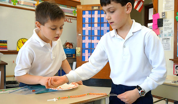 Elliott DeRose (left) and Evan Richey craft their own tri-colored rosaries using popular craft beads and twine. 