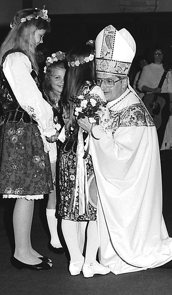 Bishop Edward M. Grosz is presented with flowers as he returns to celebrate Mass at his childhood parish, Assumption Church, on May 16, 1990.