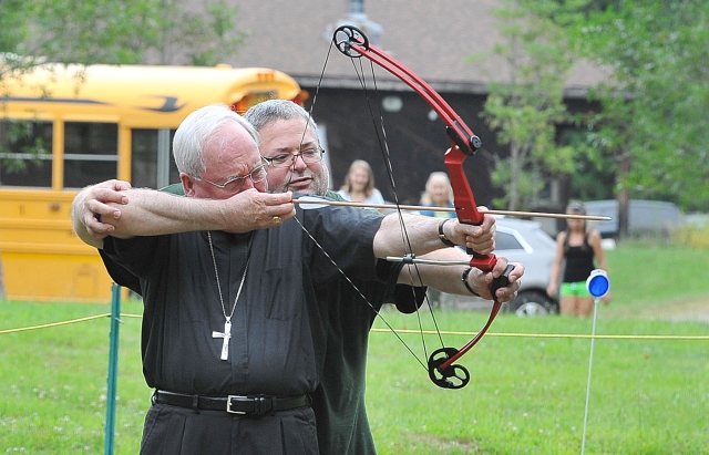 Bishop Richard J. Malone gets an archery lesson from John Mann, executive director, as the bishop makes a pastoral visit to Camp Turner in Allegany State Park. 