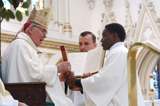 Bishop Richard J. Malone hands the Book of the Gospels to Peter Bassey during the ordination of deacons at St. Joseph Cathedral Sept. 16. The bishop presented the Book of the Gospels as a sign of the deacon's mission. (Patrick McPartland/Managing Editor)